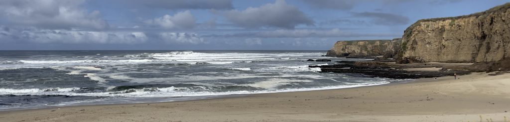 Big waves breaking on beach, with cliffs on the right side