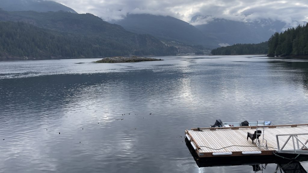 Flat body of water with mountains and clouds in background. Small boat moored at dock in lower right corner.