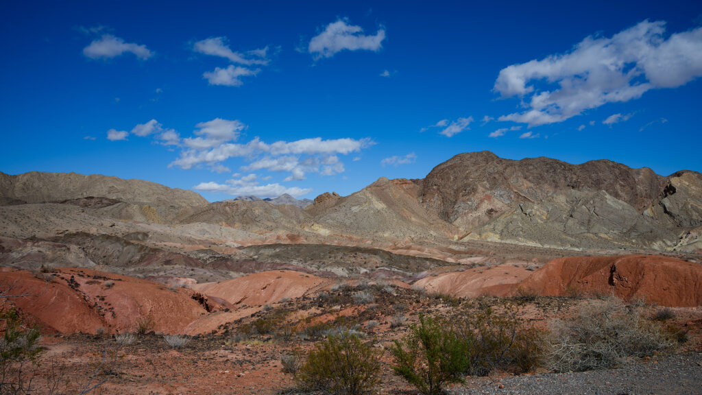 Landscape with white clouds in bright blue sky, rounded mountains and hills in red